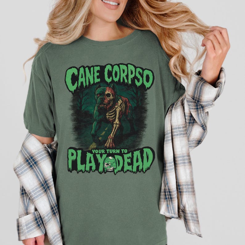 May include: Green t-shirt with the text "CANE CORPSO" in a green, spooky font. Below the text is a graphic of a dog skeleton. The text "YOUR TURN TO PLAY DEAD" is below the graphic in a green font.