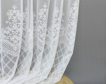 May include: A sheer white curtain panel featuring intricate white floral embroidery and a lattice pattern along the bottom edge. The fabric is lightweight and semi-transparent, with vertical folds creating a draped effect across the window covering.