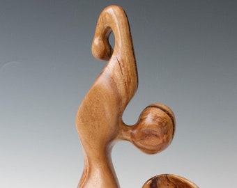 May include: Abstract wooden sculpture with a natural wood finish. The sculpture is made of a single piece of wood and has a flowing, organic shape. It is mounted on a black wooden base.