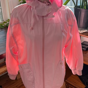 May include: A pink hooded jacket with a zip fastening and two pockets. The jacket is on a mannequin and is a light pink colour.