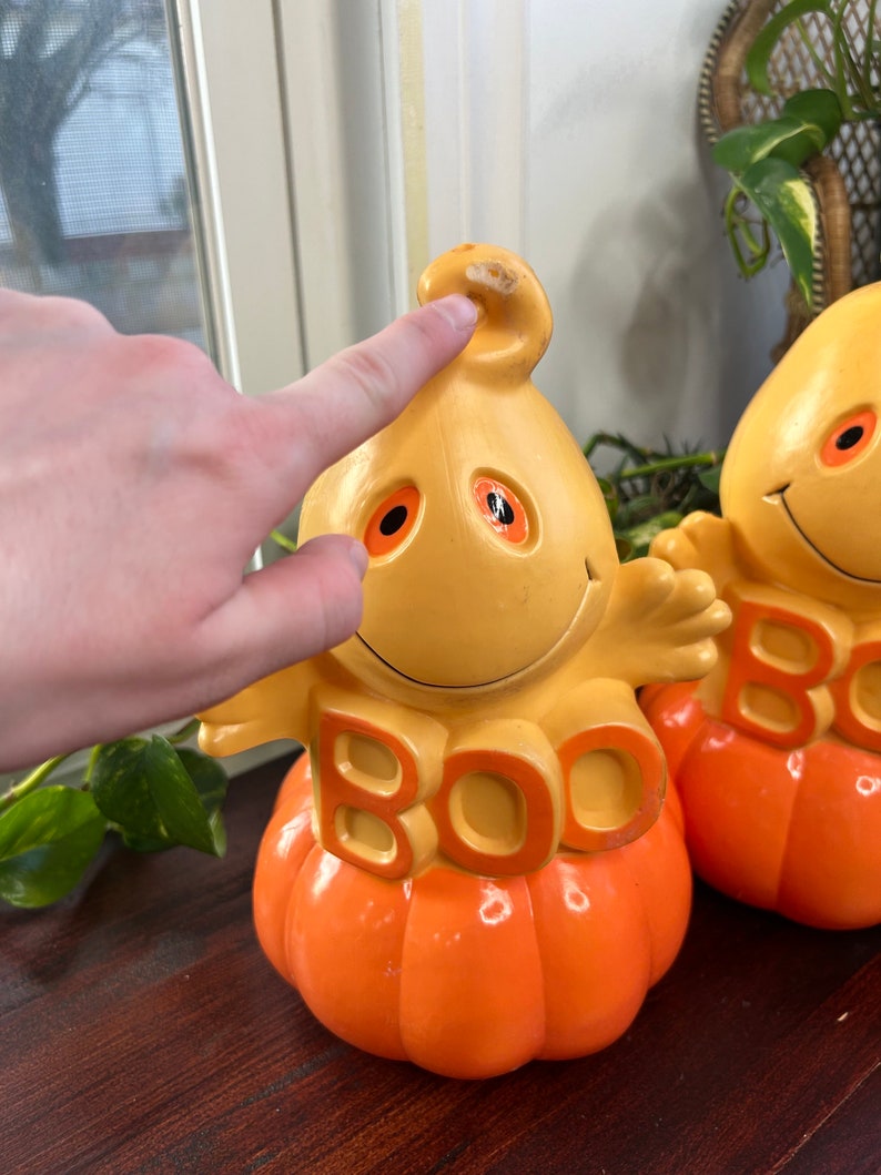 May include: Two orange and yellow ceramic pumpkin figurines with ghost faces and the word "BOO" on the front.