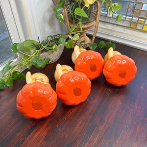 May include: Four orange and yellow ceramic pumpkins with a hole in the top. The pumpkins are sitting on a wooden surface.