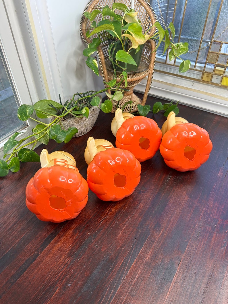 May include: Four orange and yellow ceramic pumpkins with a hole in the top. The pumpkins are sitting on a wooden surface.