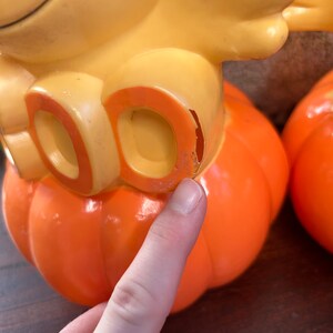 May include: Two orange plastic pumpkins with yellow bird figures on top. The bird on the left has the word "DO" on its chest.