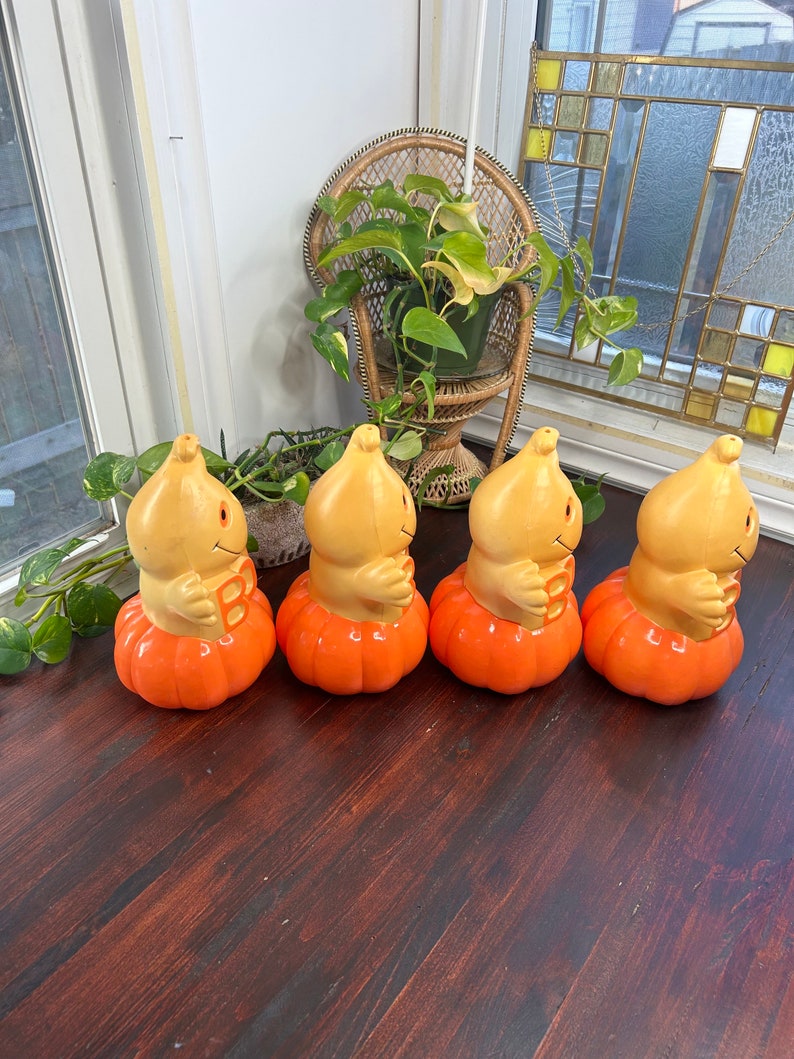 May include: Four orange pumpkin-shaped Halloween decorations with a smiling face and the letter "B" on the front. The decorations are made of plastic and have a vintage look.