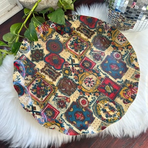 May include: A large, round, vintage serving tray with a colourful, patterned design. The tray is made of plastic and has a glossy finish. The pattern features a variety of floral and geometric motifs in shades of red, blue, yellow, and green.