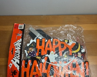 May include: A Halloween decoration with the words "Happy Halloween!" in orange letters. The decoration features images of a witch, ghost, and other Halloween-themed characters. The decoration is in a plastic bag.