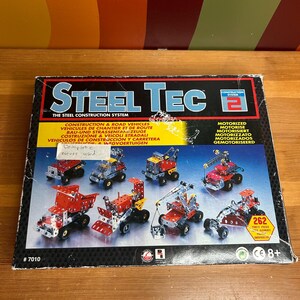 May include: A Steel Tec construction set box showing miniature construction vehicles. The box is black with red and white text, and images of the assembled models. The set includes 262 pieces and is suitable for children aged 8 and over.