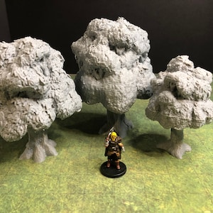 May include: Three gray 3D printed trees of varying sizes, with a textured bark-like surface. The trees are arranged on a green surface, with a miniature figure standing in front of them.