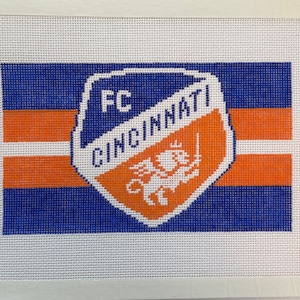 May include: A white canvas with an orange and blue striped design. The center of the canvas features a white and orange crest with the text "FC CINCINNATI" and a winged lion. The bottom right corner of the canvas has the text "LSL" in orange.