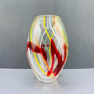 May include: Clear glass vase with colorful, swirling stripes of red, yellow, orange, white, and green. The vase has an oval shape and is likely used for decorative purposes.