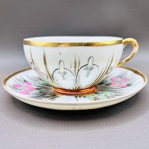 May include: White porcelain teacup and saucer set with gold trim. The cup features a swan design, and the saucer has pink and green floral accents. A classic tea set.