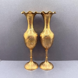 Peut inclure: Une paire de grands vases en laiton poli dotés de tiges fines, de corps arrondis et de bords évasés et festonnés. La surface de chaque vase est ornée de gravures florales délicates et complexes qui entourent la section centrale bombée.