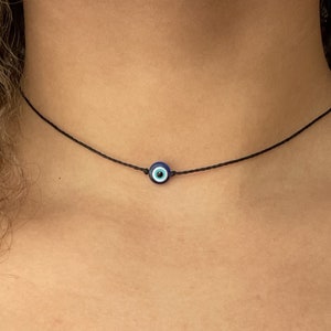 May include: A simple black choker necklace with a small blue evil eye charm.