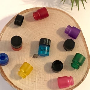 May include: Assortment of small glass bottles with various colored caps and labels. The bottles are arranged in a circle on a wooden surface. One bottle is labeled "Lavender".
