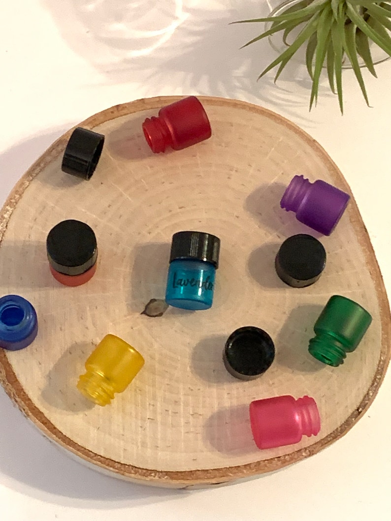May include: Assortment of small glass bottles with various colored caps and labels. The bottles are arranged in a circle on a wooden surface. One bottle is labeled "Lavender".