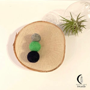 May include: Three felt balls stacked on a wooden slice. The balls are gray, green, and black.