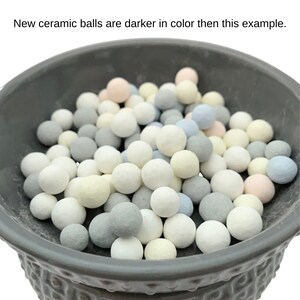 May include: A gray ceramic bowl filled with small, round ceramic balls in various pastel colors, including white, gray, blue, and yellow. The text at the top says, "New ceramic balls are darker in color then this example."
