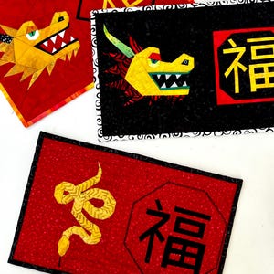 May include: Three red fabric squares with black borders and Chinese characters. The squares feature a yellow dragon, a yellow snake, and the character "福" (Fu) meaning "good fortune".