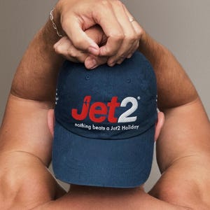 Op de afbeelding: Marineblauwe baseballcap met het Jet2-logo in rood en wit. De tekst "nothing beats a Jet2 Holiday" staat eronder. De cap heeft een klassieke stijl met een gebogen klep.