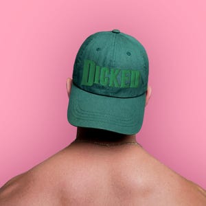 Könnte beinhalten: Eine Person trägt eine grüne Baseballkappe mit dem Wort "DICKED" in grün auf der Vorderseite gestickt.