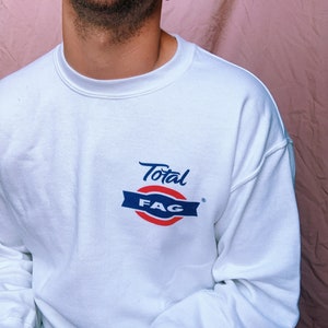May include: White sweatshirt with a blue and red logo that says "Total FAG" in a cursive font.