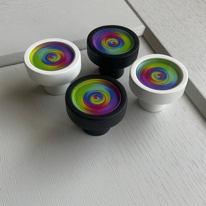 Pode incluir: Quatro botões de armário coloridos com um padrão de arco-íris em espiral. Os botões são feitos de cerâmica branca e preta com um design circular.