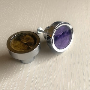 May include: Two round cabinet knobs with a chrome finish. One knob has a purple velvet insert and the other has a brown insert.