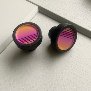 May include: Two round black knobs with a pink and orange gradient design and black stripes.