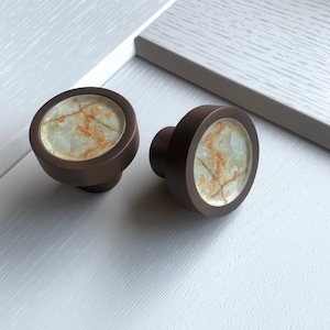 May include: Two round, bronze cabinet knobs with a white and brown marbled design.