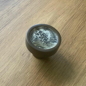 May include: A round, brown cabinet knob with a black and white animal print design.