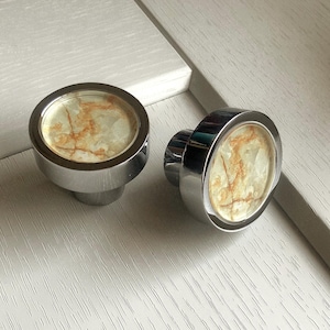 May include: Two round, chrome cabinet knobs with a marbled, beige and brown design.