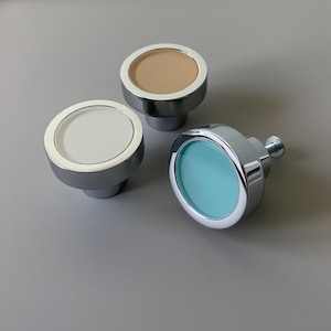 May include: Three round cabinet knobs with a chrome finish. The knobs have different coloured inserts: one is beige, one is white, and one is light blue.