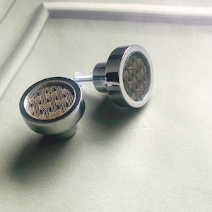 Peut inclure: Deux boutons de cabinet argentés avec un motif géométrique en or. Les boutons sont ronds et ont un bord surélevé.