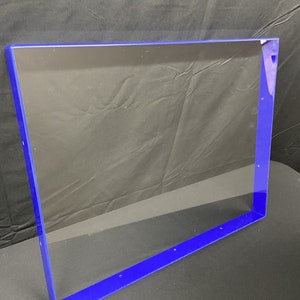 May include: A clear acrylic frame with a blue border. The frame is rectangular and has several small holes along the edges.