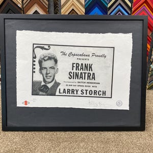 May include: A black and white framed poster advertising a performance by Frank Sinatra at the Copacabana. The poster features a photo of Sinatra in a suit and tie, with the text "The Copacabana Proudly Presents Frank Sinatra" and "Accompanied by Skitch Henderson in our Gay Spring Revue with Larry Storch".