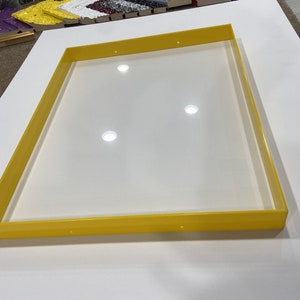 May include: A yellow plastic frame with a white background. The frame is rectangular and has a smooth surface. There are four small holes in the frame.