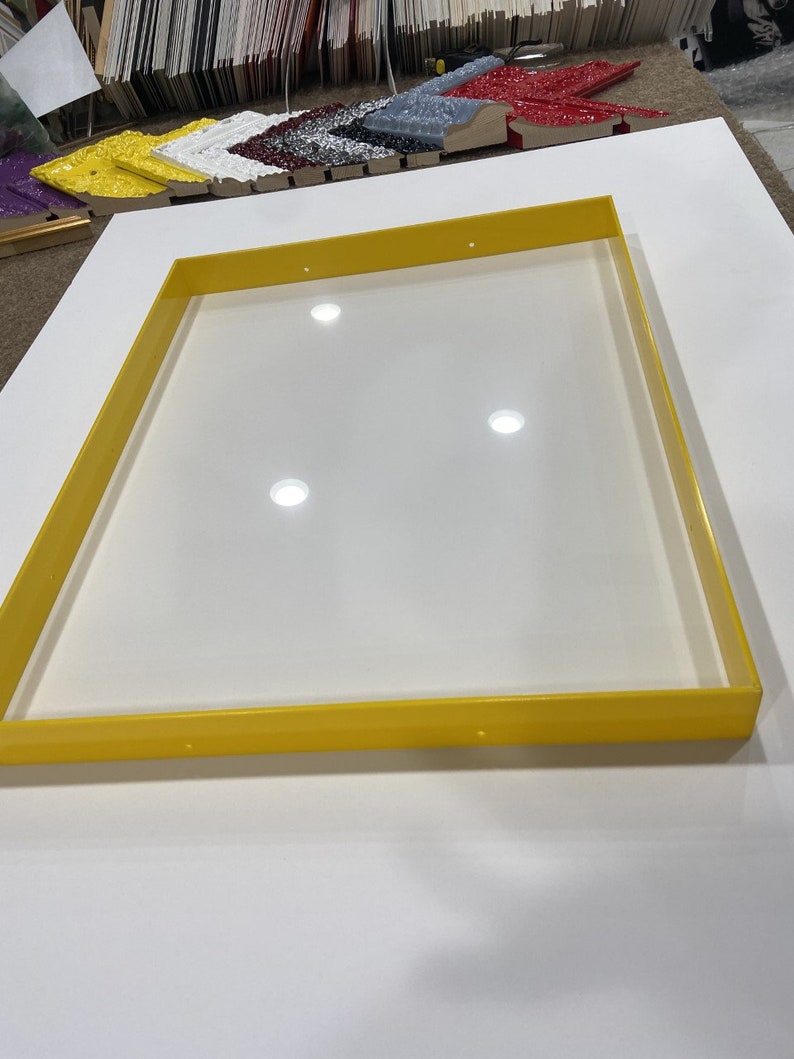 May include: A yellow plastic frame with a white background. The frame is rectangular and has a smooth surface. There are four small holes in the frame.