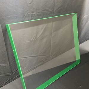 May include: A clear acrylic sheet with a green border. The sheet has several small holes along the edges.