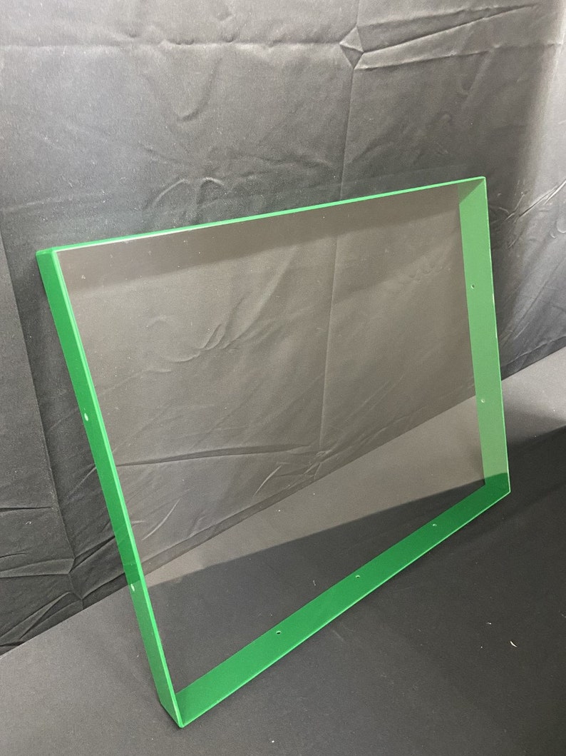 May include: A clear acrylic sheet with a green border. The sheet has several small holes along the edges.