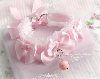 May include: A light pink choker collar featuring white lace trim, multiple satin bows, and two silver-toned metal rings. A small, round, light pink bell hangs from the center. The text "Made with Love Copyright Mycocomimi" is visible.