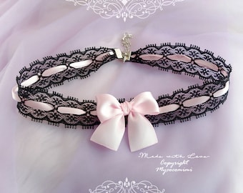 May include: A black lace choker with a pink satin ribbon bow. The choker has a delicate design with small cutouts. The ribbon bow is tied in a simple knot. The text "Made with Love - Copyright Mycocomimi" is printed on the bottom of the image.