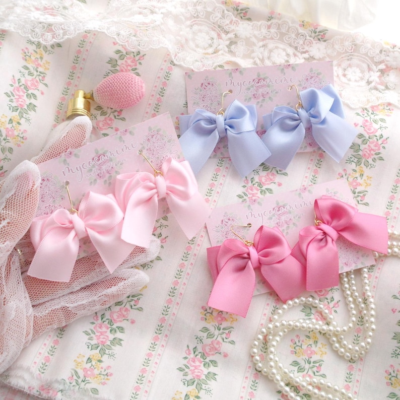 May include: Three pairs of satin ribbon bow earrings in pink, light blue, and hot pink. The earrings are displayed on white cards with the text "myceonline" printed on them.