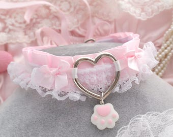 May include: Pink lace choker with a silver heart charm and a paw print pendant. The choker is made of satin ribbon and lace.