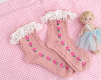 May include: A pair of pink socks with white lace trim and a floral pattern. The socks are on a pink and white gingham background.