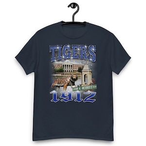 May include: Navy blue t-shirt with a graphic of a tiger, a building, and the text "TIGERS 1912" in a blue and white font.
