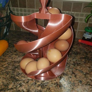 May include: A brown plastic egg holder in a spiral design, holding several brown eggs. The egg holder is designed to hold a dozen eggs. The eggs are light brown in colour. The egg holder is on a kitchen countertop.