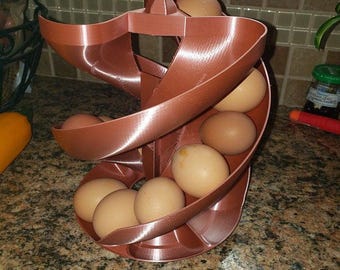 May include: A brown plastic egg holder in a spiral design, holding several brown eggs. The egg holder is designed to hold a dozen eggs. The eggs are light brown in colour. The egg holder is on a kitchen countertop.