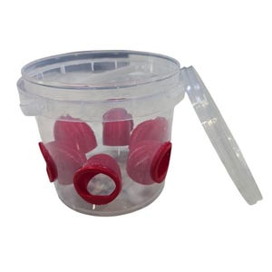 Może przedstawiać: Przezroczysty plastikowy pojemnik z pokrywką, zawierający kilka czerwonych przedmiotów w kształcie stożka. Pojemnik ma cylindryczny kształt z czerwonymi otworami po bokach. Pokrywka jest częściowo otwarta.