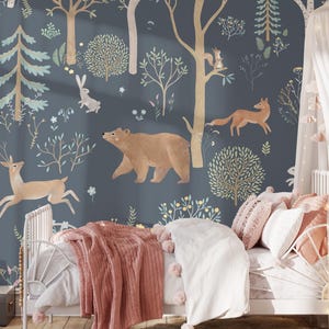 May include: A blue and white wallpaper with a woodland theme. The wallpaper features a bear, a deer, a fox, and a rabbit. The wallpaper is in a child's bedroom with a white bed and pink bedding.